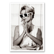 Zwart-wit foto van Brigitte Bardot met witte zonnebrillen en een sigaret tussen haar lippen, terwijl ze speels haar handen gevouwen houdt.